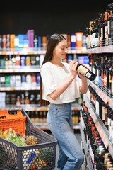 Pretty young woman in casual clothes chooses wine in the supermarket