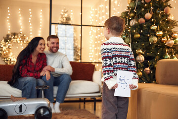 Dear Santa, boy is holding letter. Happy family celebrating new year together at home