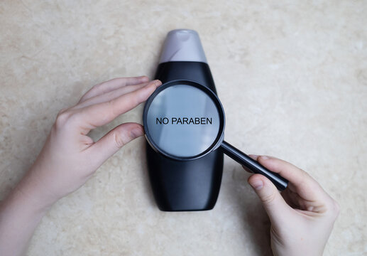 Female hands holding a can of shampoo, where it is written paraben free, no paraben. The concept of safe composition of shampoo without aggressive components