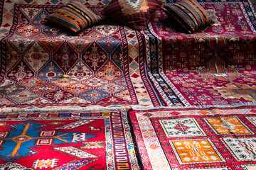 Colorful handwoven carpets with intricate geometric patterns are spread on the ground, accompanied...