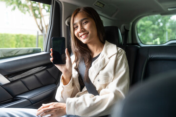 Asian Woman Traveler sitting in car back seats using smartphone call taxi service in application. Online app with cell phone and put on safety belt. Female passenger in car traveling to destination.