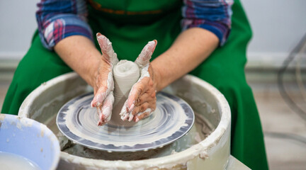 Hands shaping a clay vessel on a pottery wheel, surrounded by a messy workspace. The focus is on the craft and precision, highlighting the art of pottery making in a serene, creative environment.