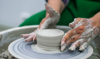 Hands shaping a clay vessel on a pottery wheel, surrounded by a messy workspace. The focus is on the craft and precision, highlighting the art of pottery making in a serene, creative environment.