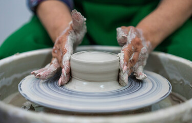 Hands shaping a clay vessel on a pottery wheel, surrounded by a messy workspace. The focus is on the craft and precision, highlighting the art of pottery making in a serene, creative environment.