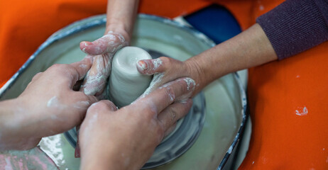 A teaching moment in pottery, where experienced hands guide and shape clay on the spinning wheel....