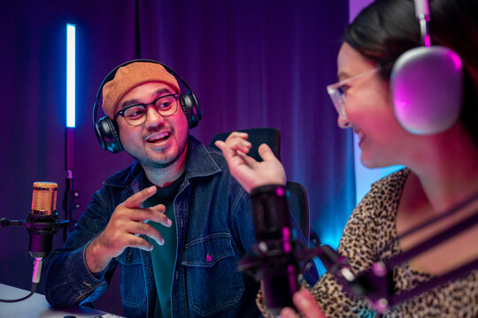 Young asian man and woman host streaming podcast with condenser microphone work on tablet at home broadcast studio. Content creator blogger recording voice over radio interview guest conversation