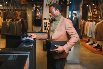 Happy african shopper holding boxes of new clothes or shoes and paying with credit card