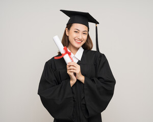 Happy asian woman in graduation costume with cap holding diploma on isolated background. College...
