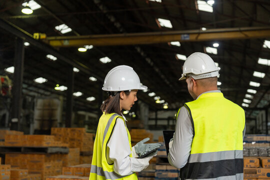 Professional engineer and technician wearing safety helmet analyzing meeting with tablet in factory warehouse. Confident factory workers group inspection industry factory. Teamwork concept.