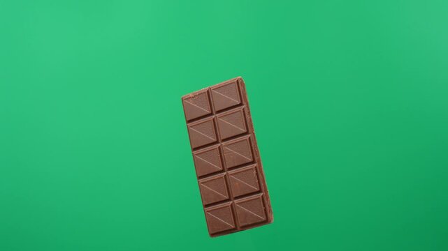 A chocolate bar is rotating on a green background. A chocolate bar close-up.