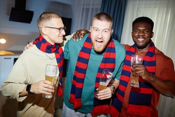 Waist up portrait of three cheerful sports fans wearing matching team scarves and holding beer...