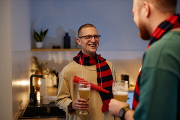 Waist up portrait of smiling sports fan talking to friend during after game party in home kitchen