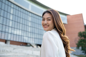 Fototapeta premium Portrait beautiful Businesswoman in suit standing at the buildings downtown. Confident woman looking towards their goals for success. Executive Smart businessman