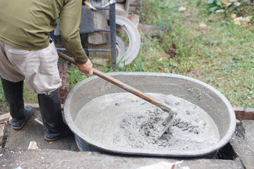 Close up worker using a hoe to mix cement powder, sand, stones in basin for mixing cement. Concept. Construction worker job. Hard working. Process of construction work with cement        