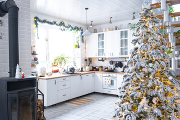 Christmas decor in white kitchen, modern rustic interior with a snowy Christmas tree and gold fairy lights. New Year, Christmas mood, cozy home.