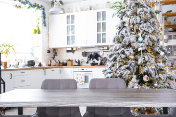 Grey Wooden empty table to demonstrate product with space for text with upholstered chairs in white kitchen, modern interior with Christmas tree and fairy lights. New Year, Christmas mood, cozy home.