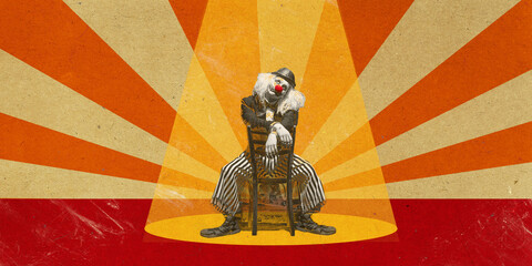 Circus clown seated on chair under glowing spotlight with radiant orange beams. Vintage theatrical...