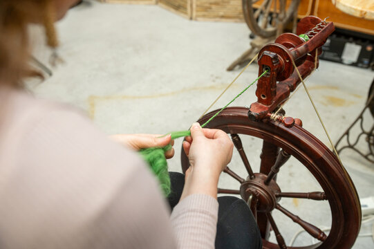 Distaff Day Caucasian female adult spinning yarn on traditional wheel in workshop - Powered by Adobe