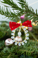 Christmas tree ornament with red bow and beads hanging on pine branch
