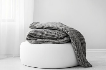Cozy gray knitted blanket on white ottoman in minimalist living room interior