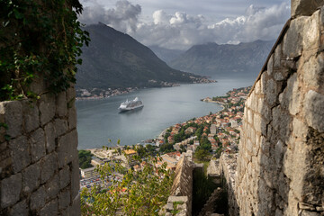 Scenic Spot of The Old Kotor Fort Trail. Cruise ship naturally surrounded by a frame of defensive walls. Rays reflecting in the water. The sunlit city of Kotor, Montenegro, Balkans. 