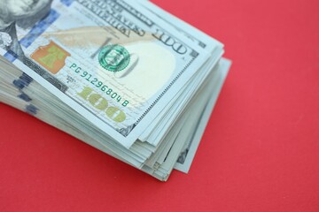 Big amount of hundred dollar bills in thick stack lies on bright red color paper background