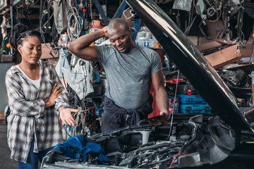Mechanic Explains Car Repairs to a Woman in a Busy Workshop During the Day