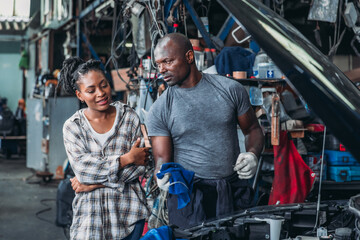 Man Explaining Car Repair to Woman in Busy Automotive Workshop During Daylight Hours