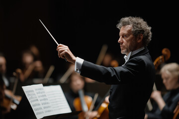 Focused orchestra conductor leading musicians during performance