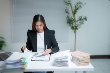 Asian businesswoman reviewing documents and working with financial chart using laptop at office desk, busy worker analyzing financial reports, business and finance concept