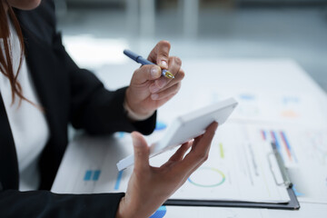 Businesswoman in a suit analyzing financial charts while using a calculator, performing detailed calculations and evaluating company performance for strategic planning and growth