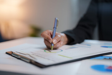 Businesswoman analyzing financial charts and diligently making notes on a clipboard, engaged in document review, using a pen for precise writing, capturing essential data