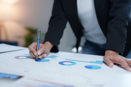 Businesswoman reviewing financial reports, pointing at pie charts and bar graphs with a pen, analyzing data and making notes during a business meeting