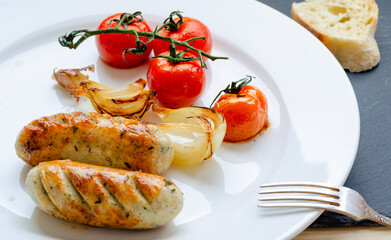 Grilled fried sausages on a white plate with homemade vegetables.