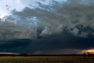 Wieczorne niebo pokryte ciemnymi, burzowymi chmurami. Na linii horyzontu widać smugę padającego deszczu. Widać tam przejaśnienia rozświetlone promieniami zachodzącego słońca. © boguslavus