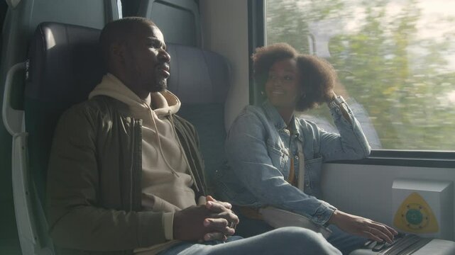 Passengers, a young African American woman, and a man having a friendly conversation during a train travel around Europe, handheld shot.