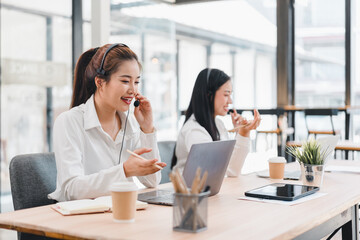 Two women working in modern office with laptops and headsets