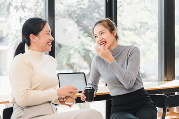 Two women laughing and chatting over coffee in bright cafe