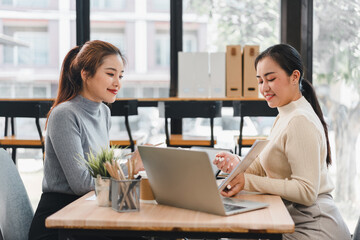Two women discussing work at laptop in modern office
