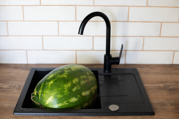 a large juicy watermelon lies in a kitchen black sink with a wooden countertop, washing and hygiene...