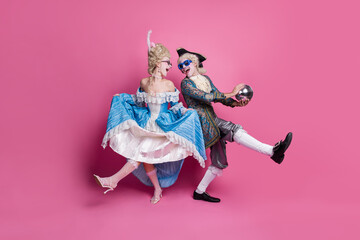 Elegant couple in vintage costumes celebrating a vibrant masquerade against a pink backdrop