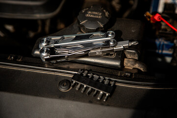 A multi-tool with various attachments is placed on a car engine, highlighting its utility for automotive repairs, with a set of interchangeable bits nearby