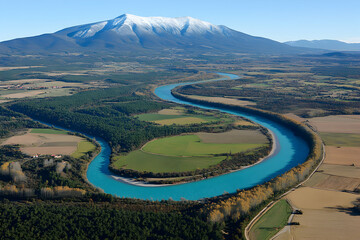 Fototapeta premium Aerial view of a turquoise river meandering through a valley, with snow-capped mountains in the background. Stunning landscape photography showcasing nature's beauty.