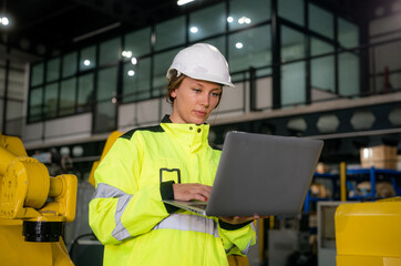Woman in safety gear using laptop in industrial facility during daytime work