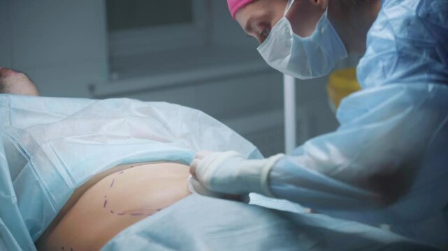 A surgeon prepares to make an incision on the abdomen of a patient lying on the operating table, surrounded by surgical instruments in a sterile environment.