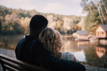 Couple in love sitting on park bench and looking at water, back view