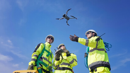 Team of Professionals Operating a Drone in Bright Yellow Safety Gear on a Clear Day