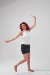 A woman with red hair poses for the camera with a smile on her face, she is wearing a white T-shirt and a black skirt. She has a beautiful figure. Fitness and healthy eating concept.
