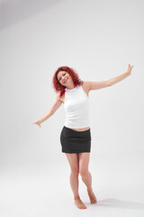 A woman with red hair poses for the camera with a smile on her face, she is wearing a white T-shirt and a black skirt. She has a beautiful figure. Fitness and healthy eating concept.