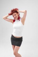 A woman with red hair poses for the camera with a smile on her face, she is wearing a white T-shirt and a black skirt. She has a beautiful figure. Fitness and healthy eating concept.